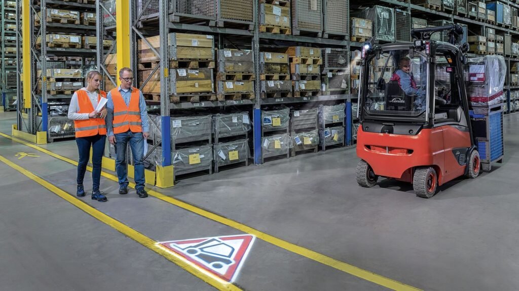 Dva radnika zastaju u skladištu upozorena svetlosnim signalom na podu emitovanim iz Linde truckspot sitema