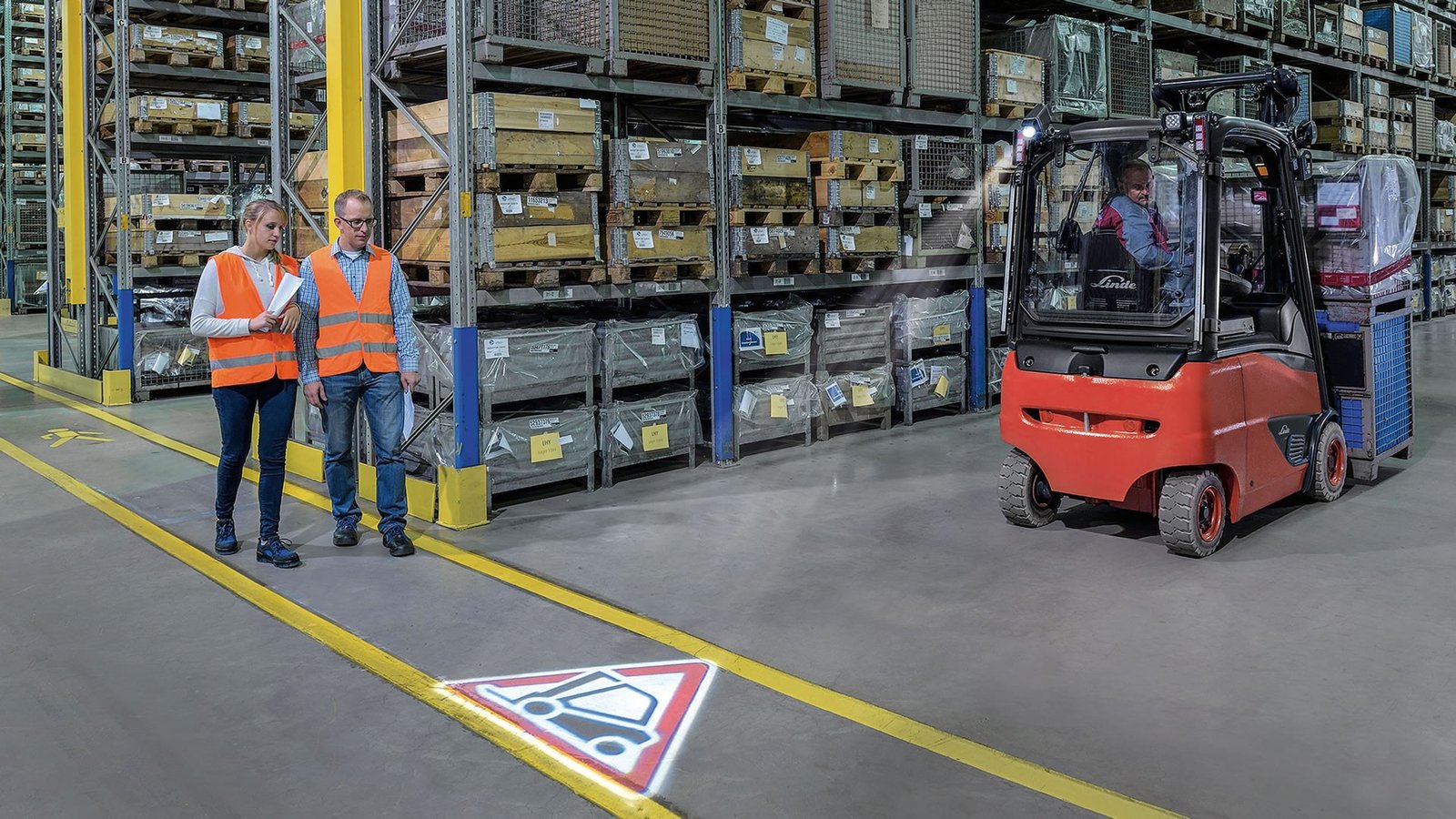 Linde TruckSpot projektuje svetlosni simbol upozorenja na pod ispred viljuškara dok pešaci prolaze skladištem