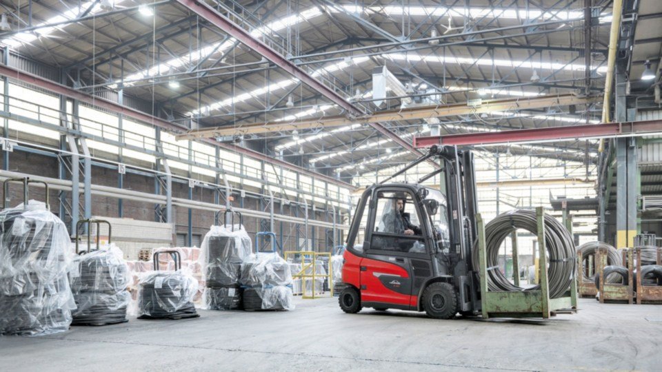 Linde viljuškar u zatvorenom skladištu prenosi metalne kalemove, okružen industrijskom opremom i ambalažom